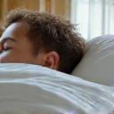 Una persona che dorme serenamente in un letto accogliente con lenzuola bianche e illuminazione soffusa, simboleggiando un sonno profondo e ristoratore.